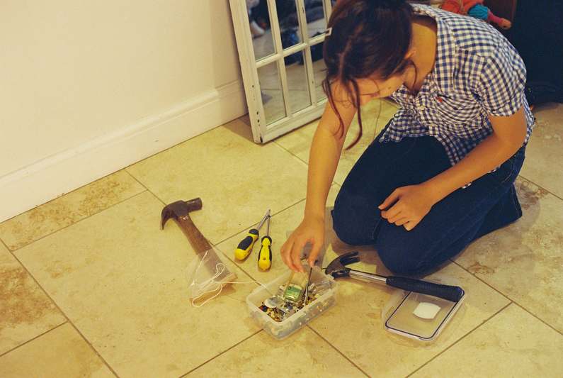 Close-up of a compact, labeled DIY toolkit with pliers, screwdrivers, and a multimeter on a concrete garage floor